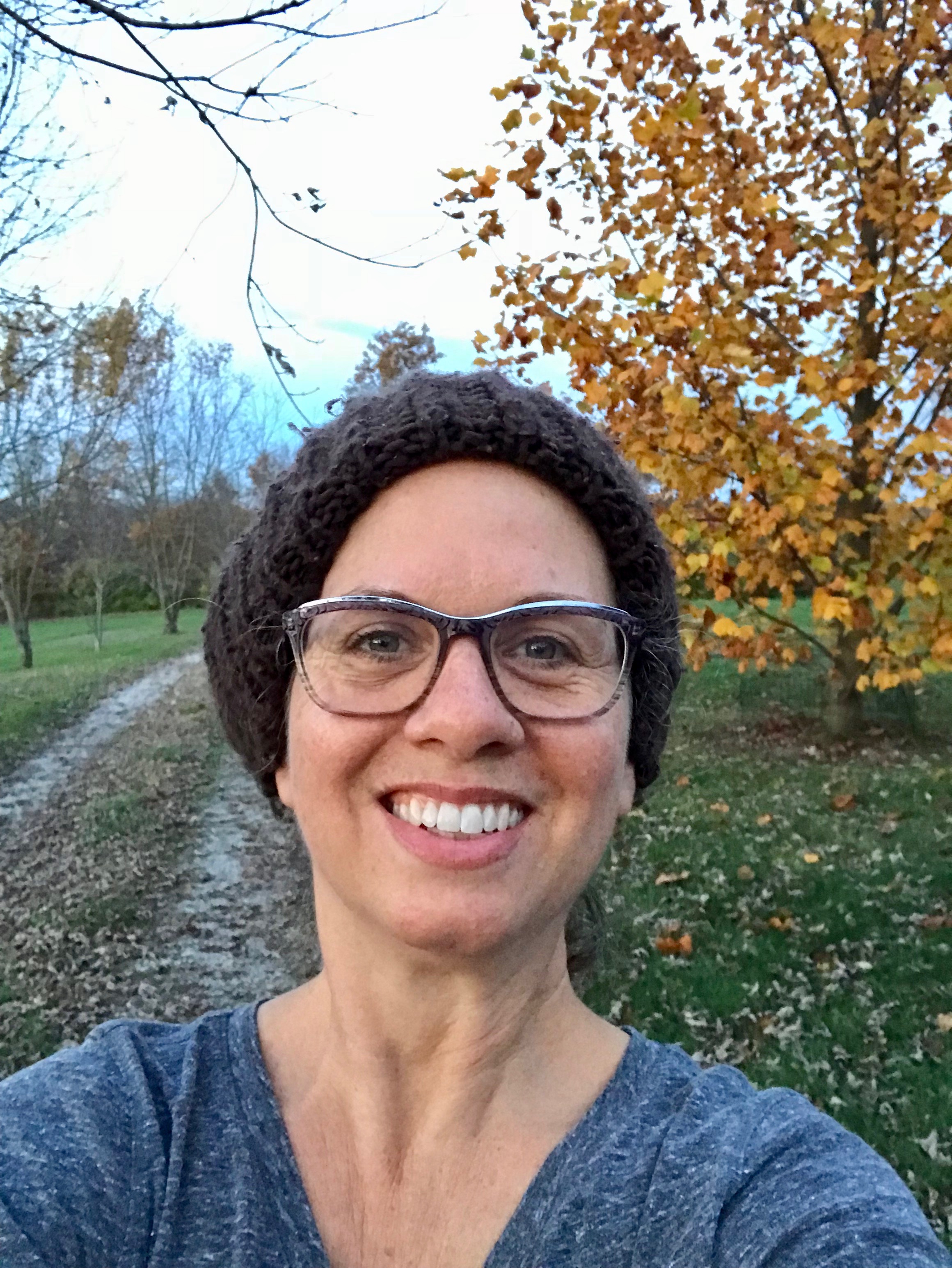 Your Creative Chord host, coach, author, poet, composer/pianist/vocalist smiling in front of a vibrant yellow tree in autumn.